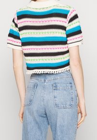 Häfven kortärmad topp med flerfärgade ränder (blå, svart, rosa, grön) och fransar i nederkant. Bärs med högmidjade ljusa denimjeans.