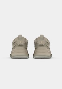 Beige athletic shoes featuring a textured mesh upper, curved design, and rear pull tabs. Translucent rubber soles add support and grip.