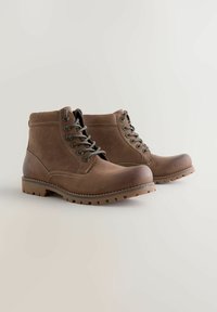 Bruna läderankelboots med rundade tår, grå snören och gummisålar med mönster. Har kontrasterande sömmar och en robust design.