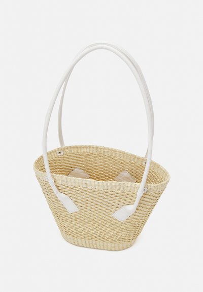 Woven straw basket with white leather handles, tapered shape, and light beige color. Features two decorative fabric accents inside.