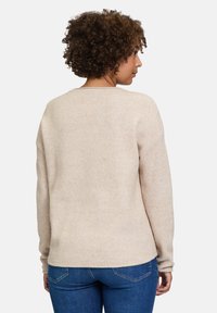 Beige Strickpullover mit strukturiertem Muster, Rundhalsausschnitt und langen Ärmeln, kombiniert mit blauen Jeans.