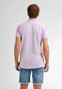 Světle fialová polo košile s krátkým rukávem, vrstveným límcem a volným střihem, doplněná o denimové šortky s ohrnutým rukávem.