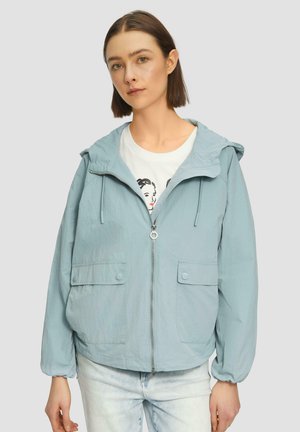 Lichtblauwe, ritssluiting jack met een capuchon, twee voorkruiszakken, elastische manchetten en een relaxte pasvorm. Gedragen over een witte T-shirt met een grafisch ontwerp.