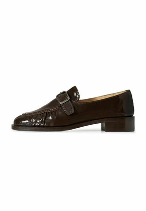 Mocasín de cuero marrón oscuro con hebilla plateada, tacón bajo y detalles cosidos sobre fondo blanco.