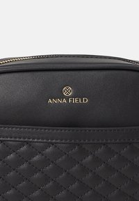 Borsa a tracolla nera trapuntata in pelle sintetica, con logo dorato impreziosito su materiale liscio e dettagli in zip dorata.