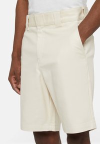 Pantaloni shorts beige realizzati in tessuto leggero, con frontale piatto, tasche laterali e cintura con passanti per la cintura. Tessuto morbido, lunghezza fino al ginocchio.