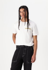 White cotton t-shirt with "QUIKSILVER" in yellow print, paired with black pants featuring white stitching and pockets.