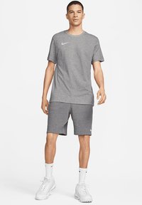 Grijze sportt-shirt met een ronde hals en korte mouwen, gecombineerd met bijpassende shorts. Bevat witte Nike-logo accenten en sportschoenen.
