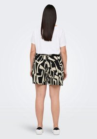 Mujer con cabello largo y liso, vistiendo una camiseta blanca lisa, pantalones cortos con un patrón abstracto en negro y beige, y zapatillas blancas, de pie mirando hacia atrás.