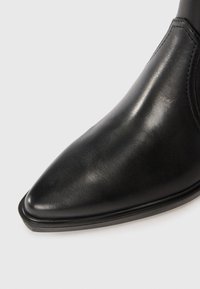 Botină neagră din piele, cu vârf ascuțit, textură netedă, strălucire subtilă și talpă plată, neagră. Detalii de cusătură pe laterale.