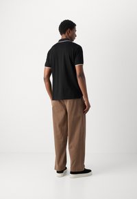 Zwarte poloshirt met witte accenten, gecombineerd met bruis met brede pijpen en zwarte sneakers met witte zolen, gezien van achteren.