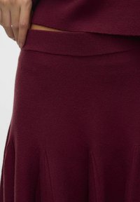 Jupe en tricot bordeaux avec une taille côtelée, une forme évasée et des coutures verticales pour plus de texture. Tissu lisse et doux.