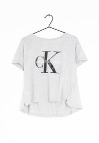 Camiseta de manga corta gris claro hecha de algodón, con un logo negro de "CK" y el texto "Calvin Klein Jeans" impresos en el frente.