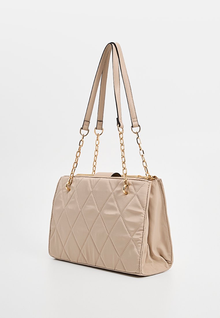Sac à main en beige matelassé avec deux poignées de portage ; dispose d'accents en chaîne dorée et d'une forme rectangulaire structurée.
