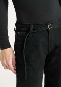 Zwarte denim jeans met een slim fit, voorzien van een riem met een zilveren gesp en een zijzak. Glad textuur en minimalistischen ontwerp.