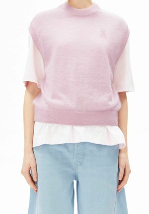 Person wearing a sleeveless pink knit vest over a white short-sleeve shirt and light blue wide-leg jeans.