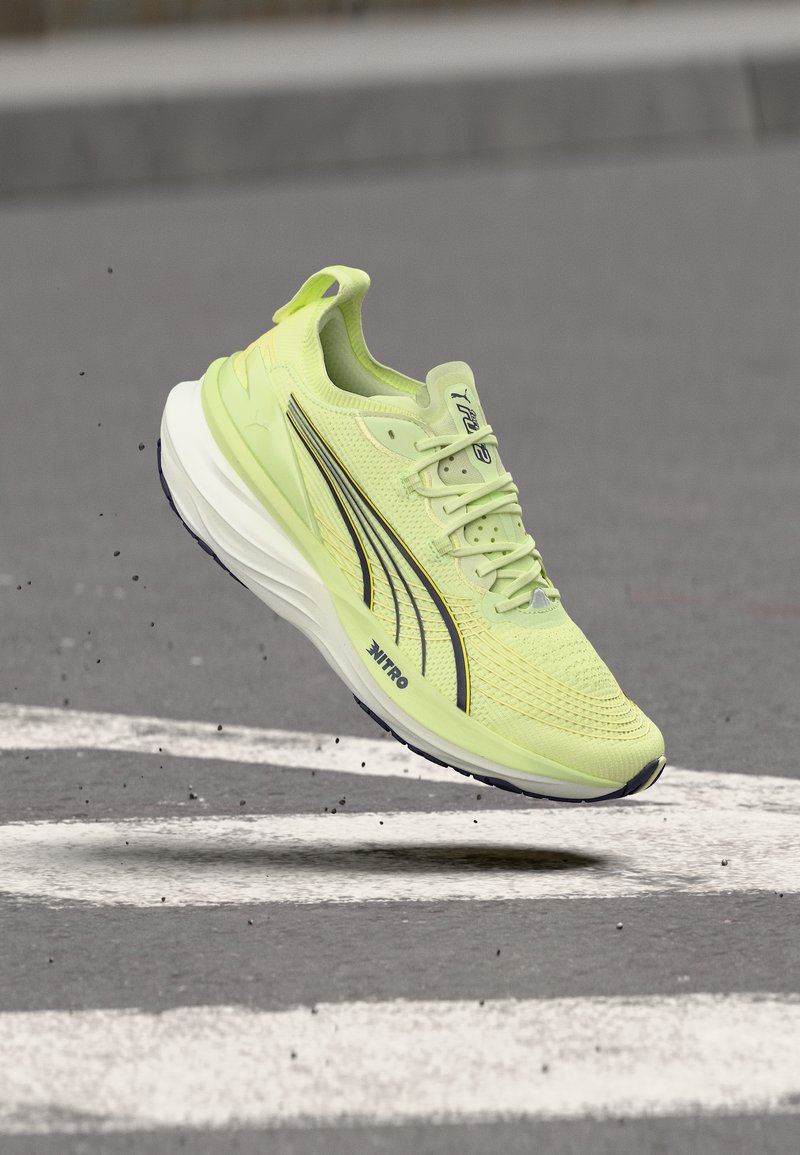 Ανοιχτό πράσινο αθλητικό παπούτσι Puma Nitro στον αέρα πάνω από άσφαλτο με λευκή βαμμένη γραμμή, που δείχνει δυναμική κίνηση και λεπτομέρειες του παπουτσιού.