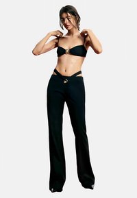 Ensemble noir deux pièces comprenant un haut bandeau avec une boucle centrale et un pantalon taille haute avec des détails découpés et une texture lisse.