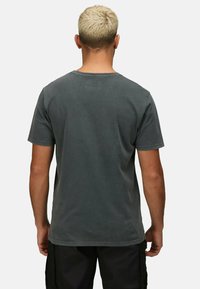 Šedé bavlněné tričko s krátkým rukávem, kulatým výstřihem a vybledlou texturou. Na zadní straně u límce je umístěno jemné logo.