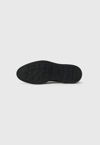 Black rubber shoe sole with textured tread patterns, featuring raised geometric shapes and a logo on the side. Flat and smooth edges.