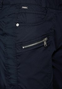 Marinblå tygbyxor med en sidoficka med dragkedja i silver, stickade detaljer och en liten märkesetikett.