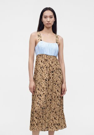 Mujer con vestido midi sin mangas con corsé fruncido azul claro y falda y tirantes con estampado de leopardo, de pie frente a un fondo blanco liso.