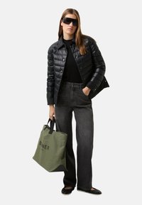 Schwarze Steppjacke, schwarzer Pullover, graue Jeans mit weitem Bein, schwarze Ballerinas und grüne Tragetasche mit schwarzem Text. Accessoires umfassen große schwarze Sonnenbrillen.