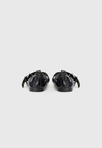 Zapatos de cuero negros con punta redondeada, cuentan con una correa de hebilla y costuras decorativas. Textura suave con un diseño minimalista.