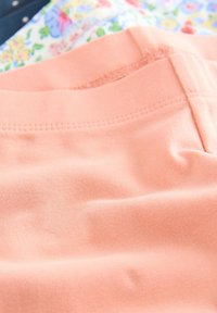 Tissu en coton de couleur pêche avec une texture lisse et une légère élasticité. L'image comprend des éléments de motifs floraux et foncés en arrière-plan.