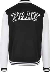 Veste universitaire noire et blanche avec corps noir, manches blanches, col et poignets rayés, et "PRAY" en grandes lettres blanches majuscules au dos.