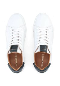Baskets en cuir blanc avec une texture lisse, accents de talon noirs contrastants et intérieur marron. Lacets et logo de la marque visibles.