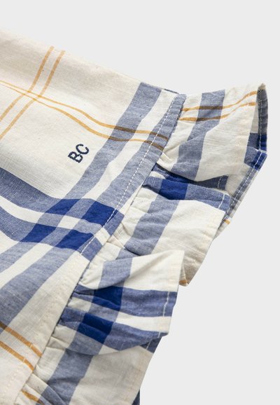 Manches courtes à volants avec motif écossais bleu, blanc et beige et initiales brodées "BC" sur tissu léger.