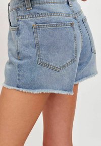 Jasnoniebieskie szorty dżinsowe z postrzępionymi nogawkami, dwoma tylnymi kieszeniami, kontrastowymi szwami i dopasowanym krojem.
