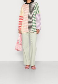 Multifarvet strikket sweater med stribede mønstre; lys grønne bukser; lyserød skuldertaske; lyserøde flethæle; afslappet pasform; forskelligartede teksturer.