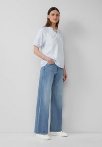 Blouse rayée bleu clair avec des manches courtes bouffantes et une fermeture à nouer, associée à un jean bleu clair ample et des baskets blanches.