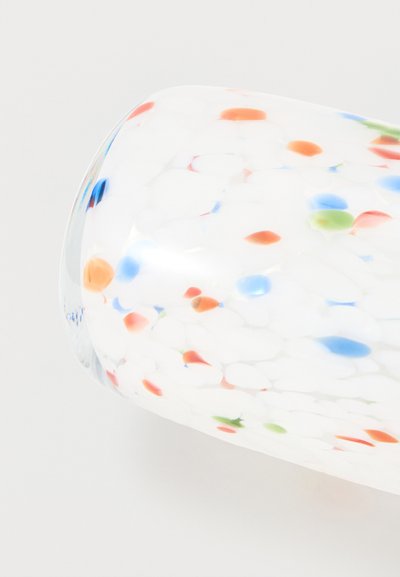 Objet en verre transparent avec des points colorés éparpillés en orange, bleu, vert et rouge à l'intérieur, reposant sur une surface blanche.