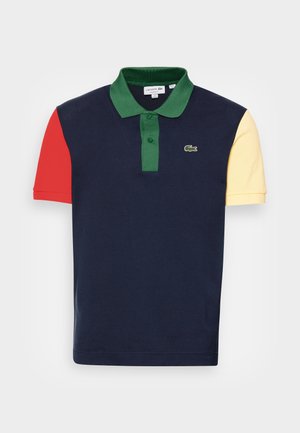 Marineblauw poloshirt met groene kraag en knoopsluiting, rode linkermouw, gele rechtermouw en klein krokodillenlogo op de borst.