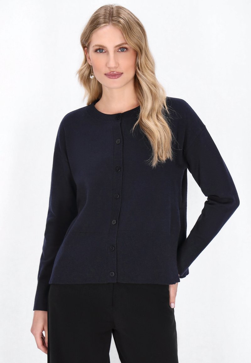 Cardigan bleumarin, fabricat dintr-un material neted, având guler rotund, tiv cu nervuri și închidere cu nasturi pe față.