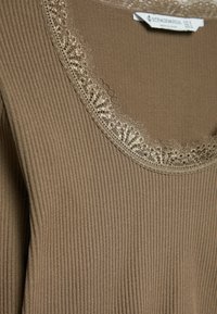 Bruine geribbelde top met een ronde halslijn en fijne kanten afwerking. De stof is zacht met een subtiele textuur. Het label draagt de naam "Stradivarius."