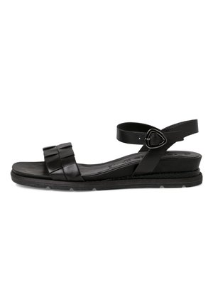 Zwarte leren sandaal met platte zool, geplooide voorstrap, enkelriem en driehoekige gesp op witte achtergrond.