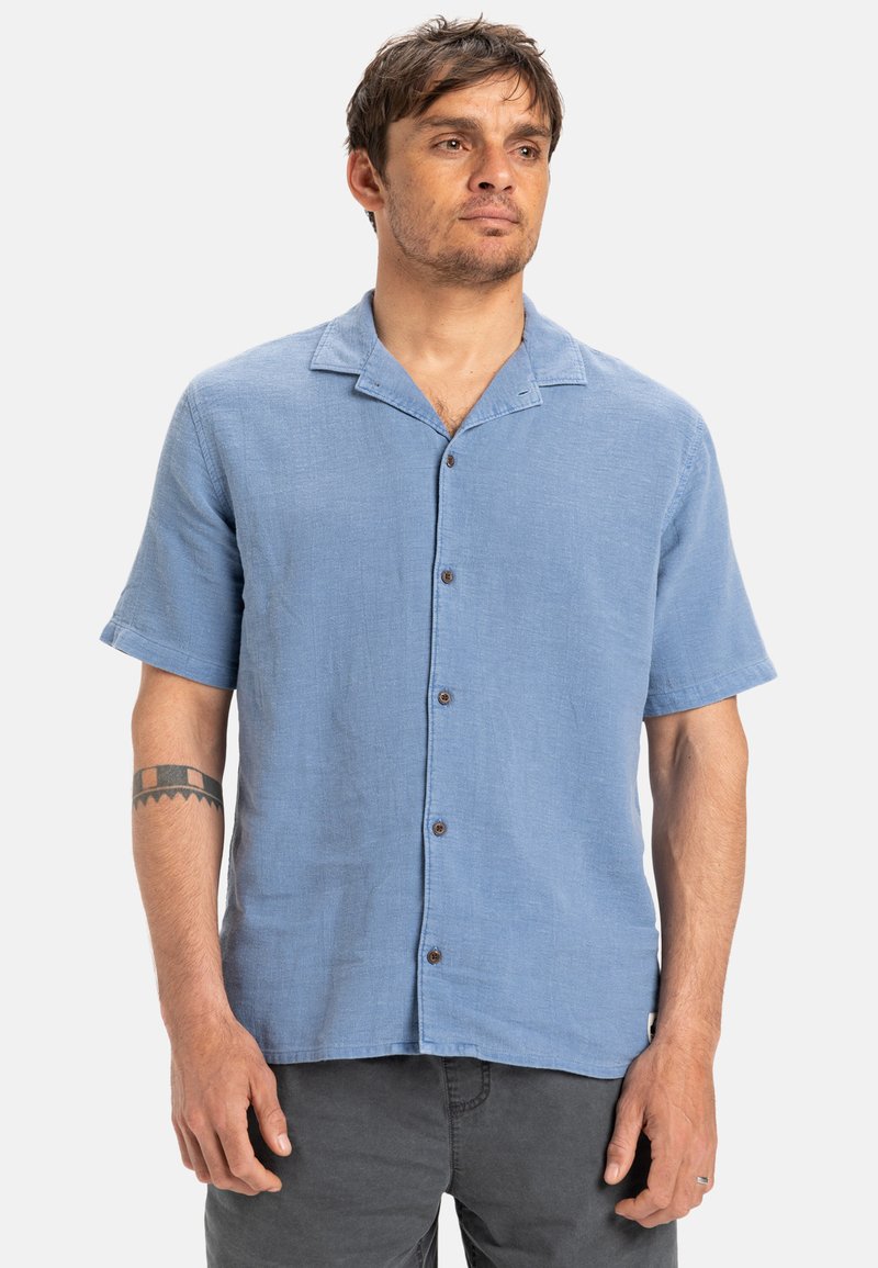 Svetlo modrá krátkopp rukávová košeľa na gombíky vyrobená z tkaniny s prešívaním, s vykrojeným golierom, hnedými gombíkmi a voľným strihom.