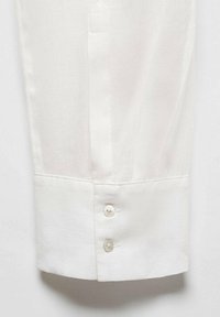 Cuff di camicia bianca a maniche lunghe con tre bottoni chiari, tessuto liscio e dettagli di cucitura sottili, che mostrano un design classico.