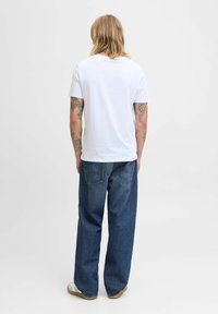 T-shirt blanc à manches courtes en coton doux, coupe décontractée ; associé à un jean en denim bleu foncé à coupe ample avec poches arrière.