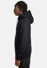 Schwarzer Hoodie mit Kängurutasche, Zugbändern, gerippten Bündchen und Saum. Der Stoff wirkt weich und hat eine glatte Textur.