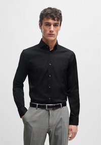 Black long-sleeve button-up shirt with a collar, smooth fabric, and black buttons, paired with light gray plaid trousers and a black belt.