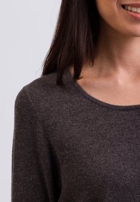 Ciemnoszary sweter z okrągłym dekoltem, dzianinową fakturą i widocznym szyciem. Materiał wydaje się miękki i lekki.