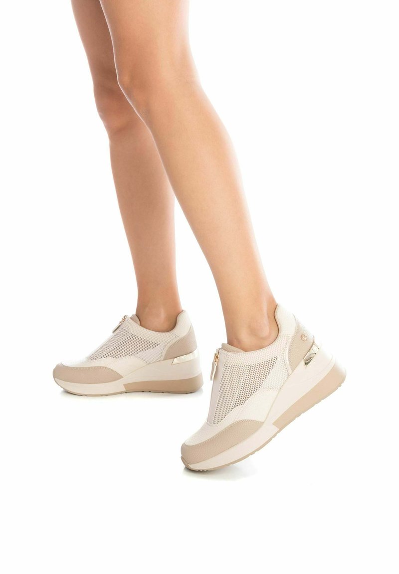Scarpe sportive beige con tomaia in rete, tacco a wedge e chiusura con zip. Presentano una texture liscia e accenti tonali a contrasto.