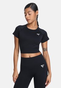 Czarny sportowy top z krótkim rękawem, skrojony na krótko, z białym logo na lewej piersi; zestawiony z dopasowanymi legginsami o wysokim stanie.