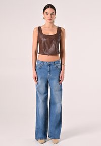 Top corto in pelle marrone con spalline larghe, abbinato a jeans a gamba larga blu chiaro con chiusura a bottoni e tasche frontali.