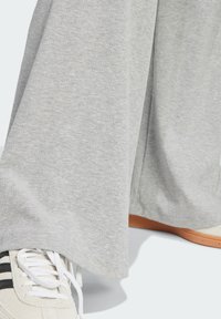 Svijetlosive, rebraste sweatpants hlače s opuštenim krojem, suptilnom teksturom i sužavajućim gležnjevima. Uparene s bijelim tenisicama koje imaju tri crne pruge.